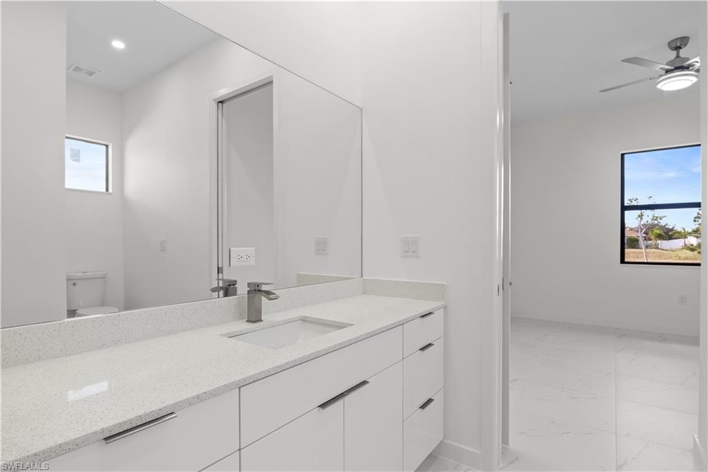 Bathroom featuring light marble finish floors, vanity, and ceiling fan