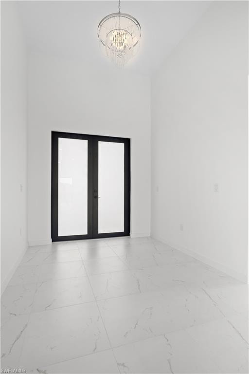 Spare room featuring light marble finish floors, french doors, and a chandelier