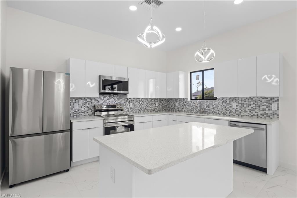 Kitchen featuring stainless steel appliances, light marble finish flooring, decorative light fixtures, white cabinetry, and modern cabinets