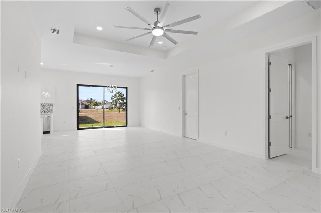 Empty room featuring recessed lighting, light marble finish flooring, a tray ceiling, and a ceiling fan