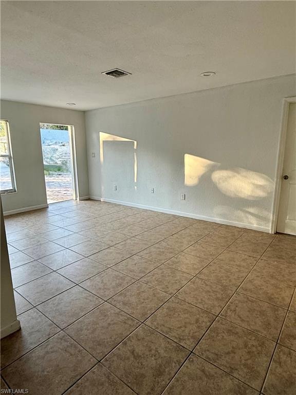 Tiled empty room with a textured ceiling and baseboards