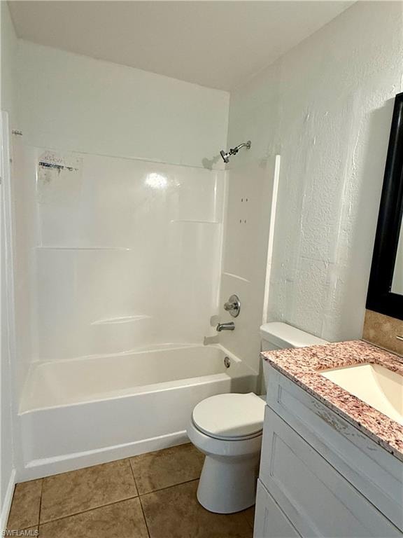 Bathroom featuring vanity, a textured wall, dark tile patterned floors, and bathtub / shower combination