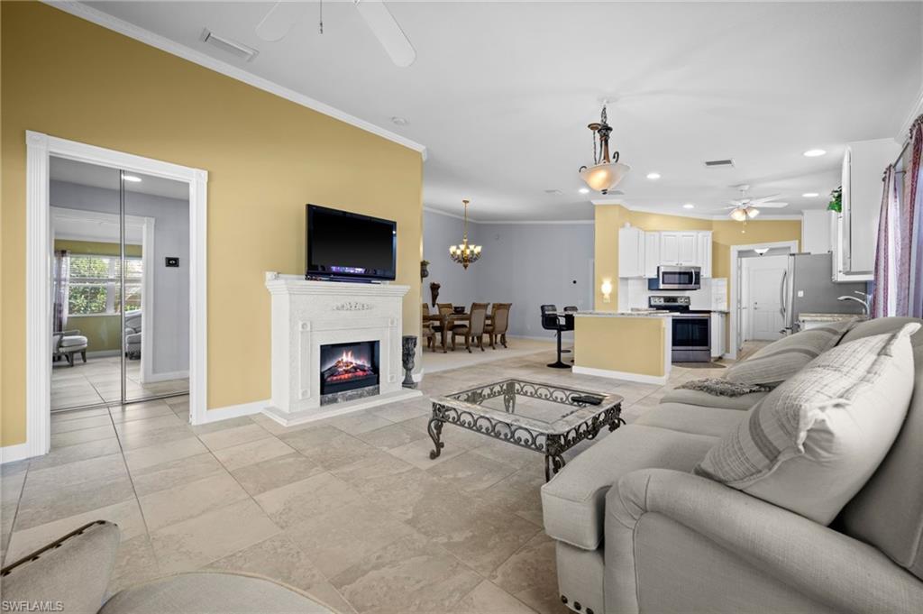 Living area with a ceiling fan, recessed lighting, crown molding, a warm lit fireplace, and a chandelier