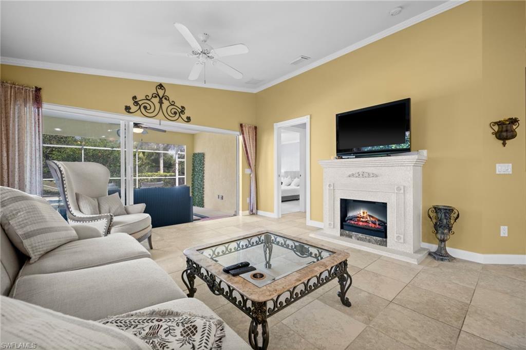 Tiled living area with crown molding, a warm lit fireplace, and a ceiling fan