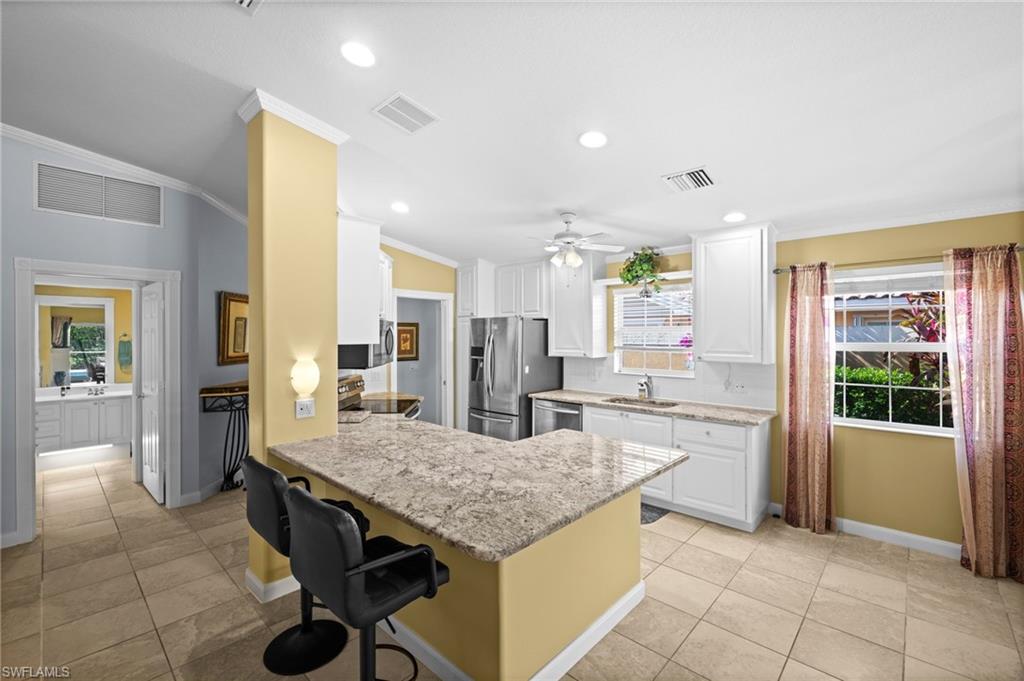 Kitchen with a peninsula, crown molding, white cabinets, a breakfast bar area, and light tile patterned flooring