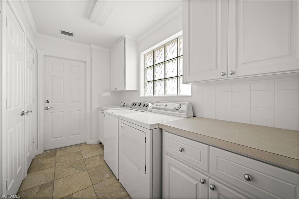 Washroom featuring ornamental molding, independent washer and dryer, and cabinet space