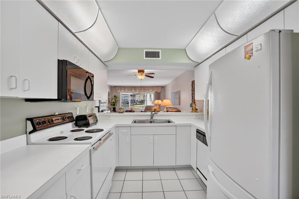 Kitchen with white appliances, white cabinets, light countertops, light tile patterned floors, and ceiling fan