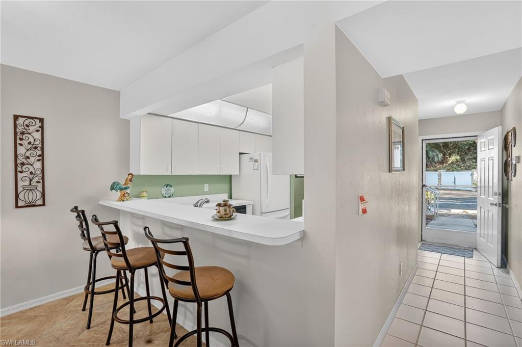 Kitchen with a breakfast bar area, light countertops, a peninsula, freestanding refrigerator, and white cabinetry