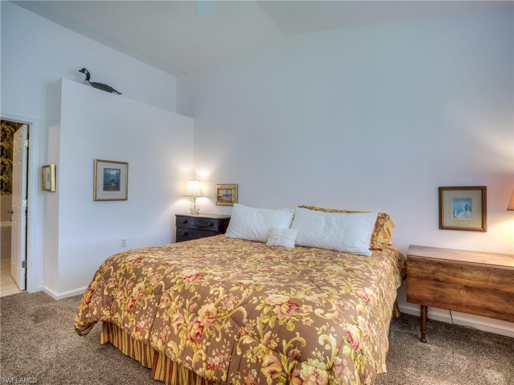 Bedroom with lofted ceiling, dark carpet, ensuite bathroom, and ceiling fan