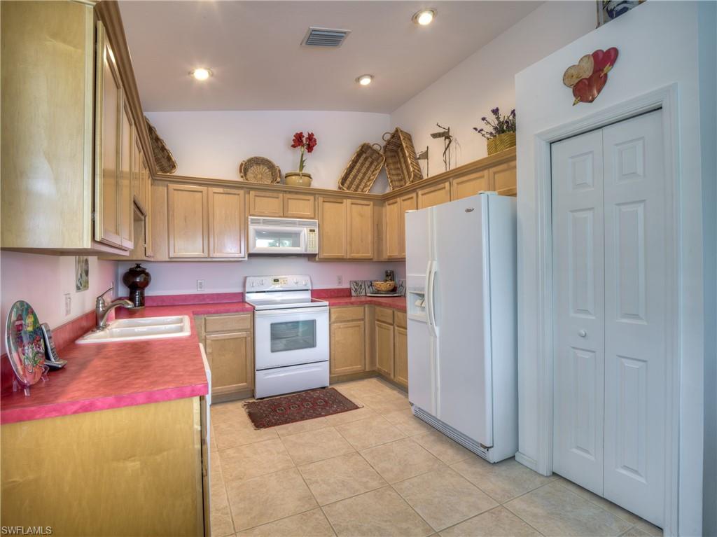 Kitchen with white appliances, vaulted ceiling, light tile patterned flooring, dark countertops, and brown cabinetry