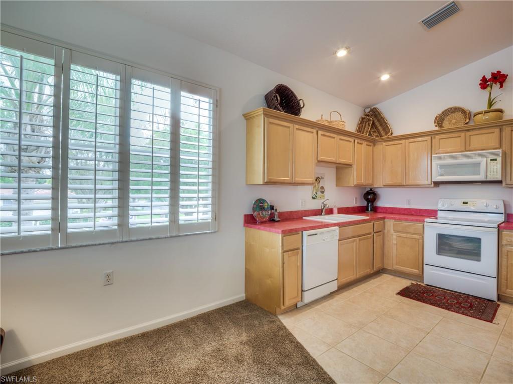 Kitchen with white appliances, lofted ceiling, light brown cabinets, light tile patterned floors, and light carpet
