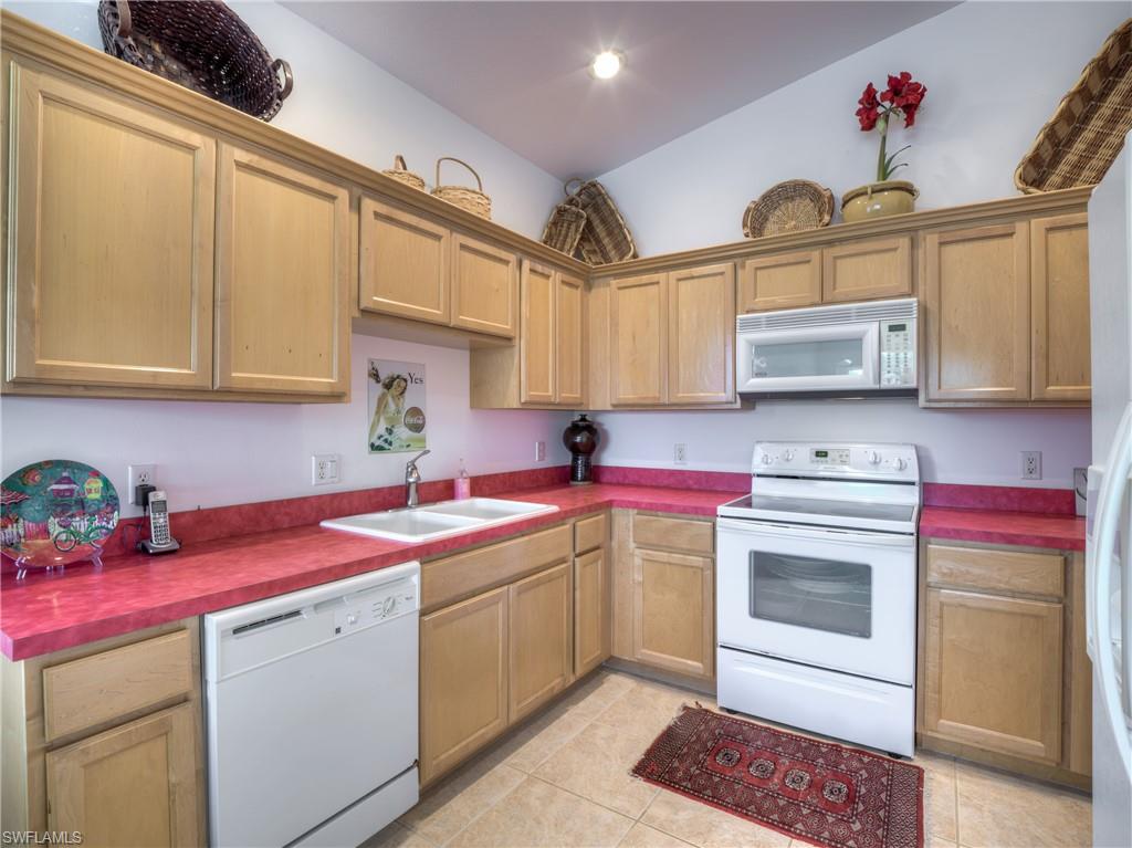 Kitchen with white appliances, dark countertops, light tile patterned floors, and lofted ceiling