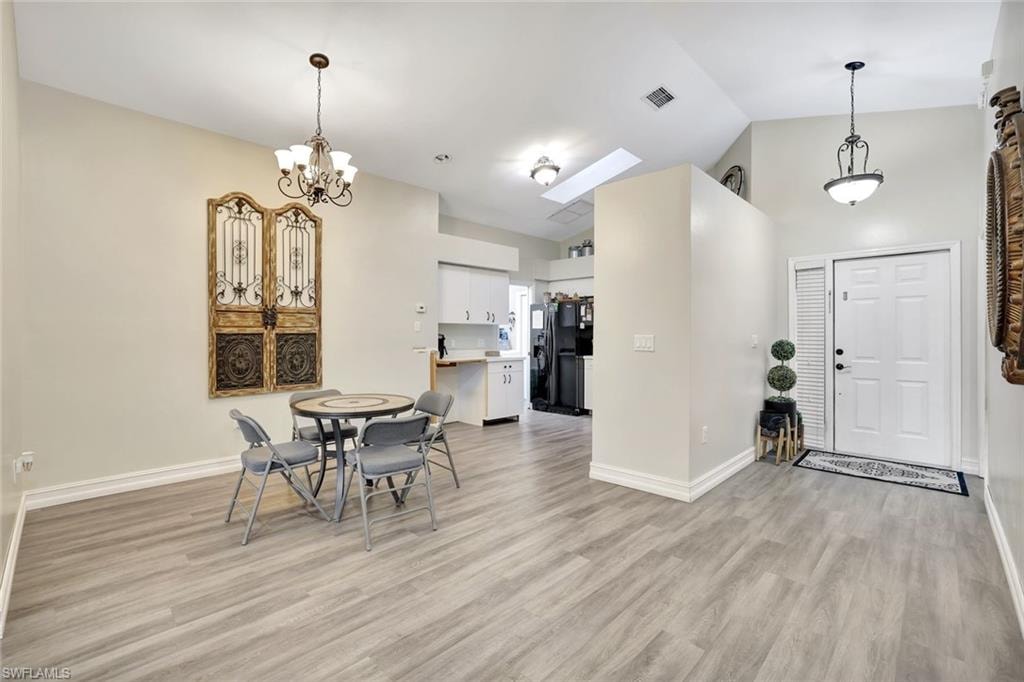 Dining space featuring high vaulted ceiling, light wood finished floors, a skylight, and a chandelier