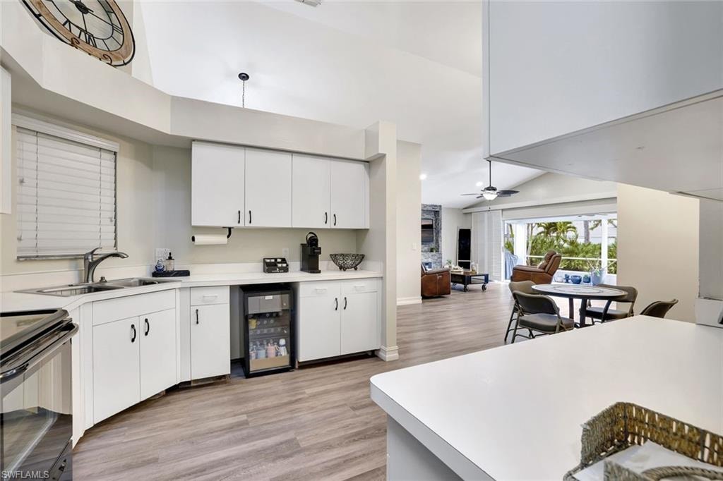 Kitchen featuring open floor plan, light wood finished floors, light countertops, beverage cooler, and high vaulted ceiling