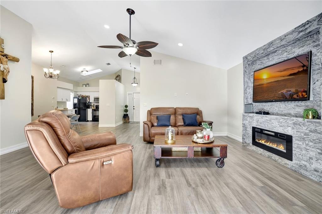 Living area with a stone fireplace, a chandelier, light wood-style flooring, a ceiling fan, and high vaulted ceiling