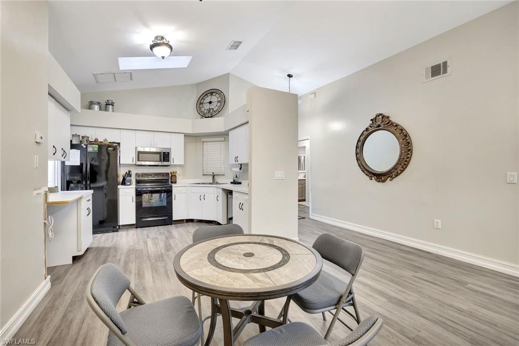 Kitchen with a skylight, light countertops, black appliances, white cabinets, and light wood-style floors