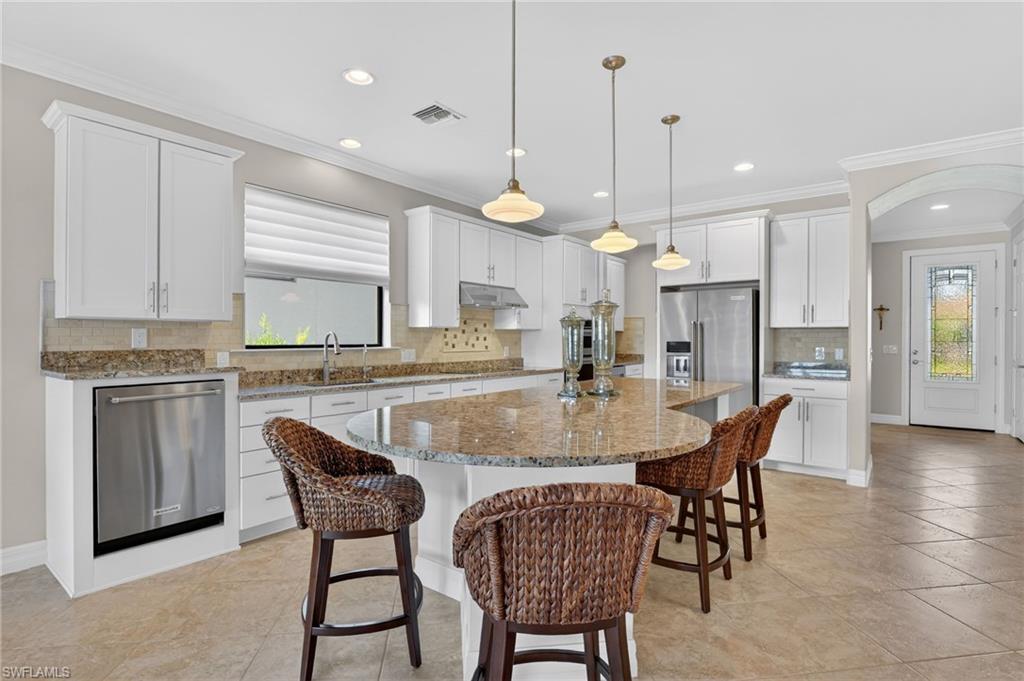 Kitchen featuring crown molding, backsplash, white cabinets, light stone countertops, and a breakfast bar area