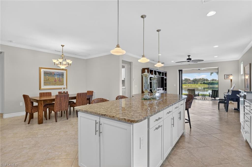 Kitchen with crown molding, a breakfast bar, white cabinetry, light stone countertops, and decorative light fixtures