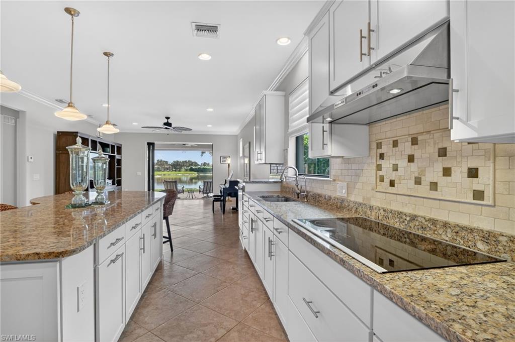 Kitchen featuring a breakfast bar area, white cabinetry, under cabinet range hood, ornamental molding, and recessed lighting