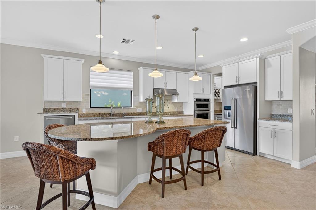 Kitchen with a breakfast bar, appliances with stainless steel finishes, crown molding, dark stone counters, and decorative light fixtures