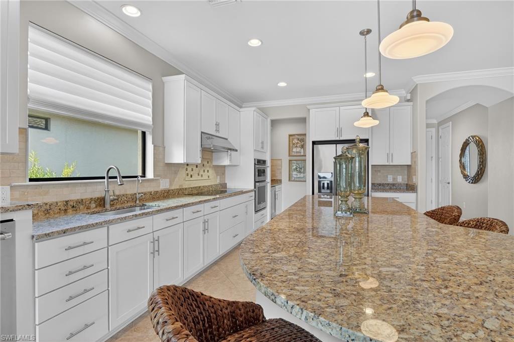Kitchen featuring a kitchen breakfast bar, light stone countertops, ornamental molding, white cabinets, and arched walkways