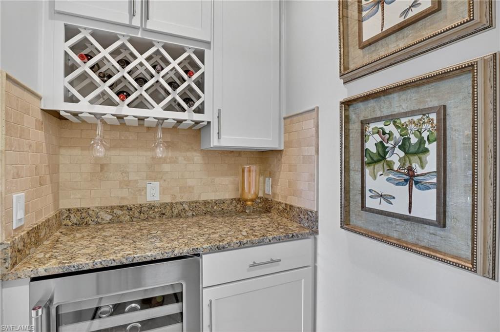 Kitchen featuring beverage cooler, white cabinetry, light stone counters, and backsplash