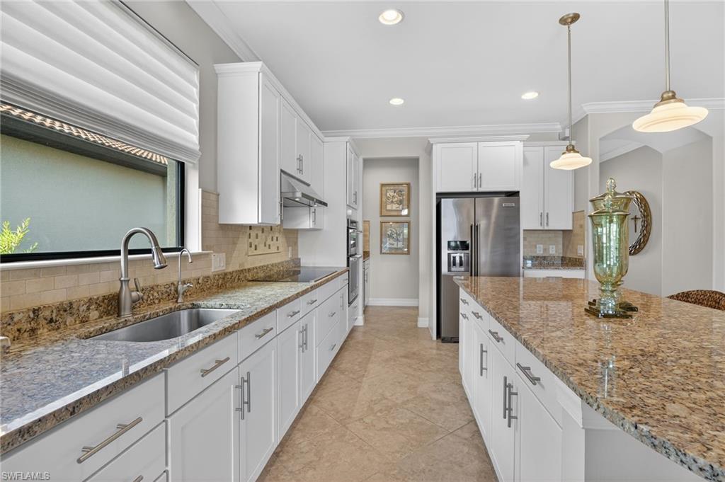 Kitchen featuring white cabinets, ornamental molding, light stone countertops, high end fridge, and hanging light fixtures