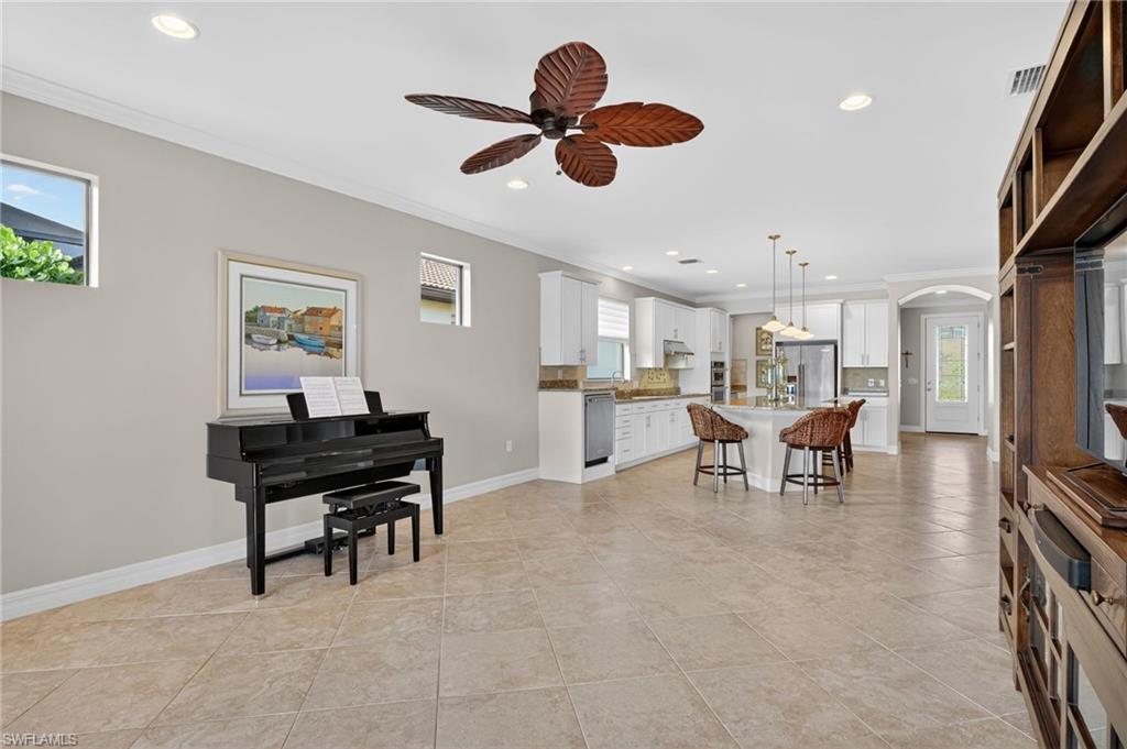 Living room with crown molding, recessed lighting, arched walkways, ceiling fan, and light tile patterned floors