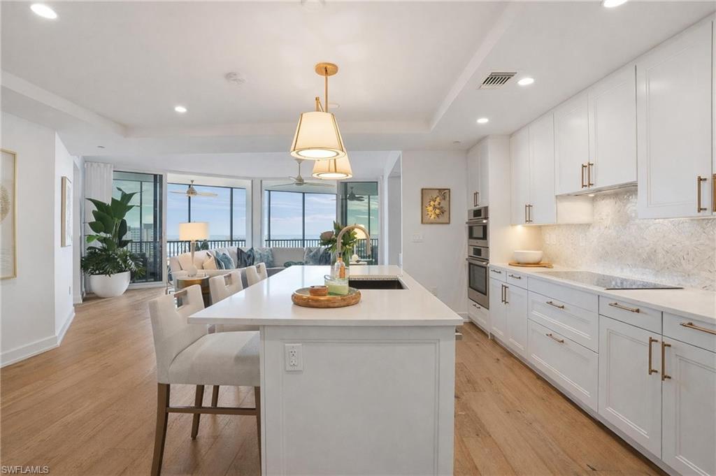 Kitchen featuring white cabinetry, open floor plan, pendant lighting, a center island with sink, and a breakfast bar area - Virtually Edited Image