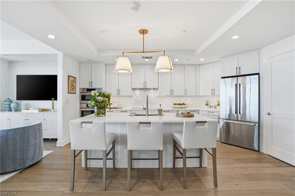 Kitchen with appliances with stainless steel finishes, white cabinets, a kitchen bar, hanging light fixtures, and an island with sink - Virtually Edited Image