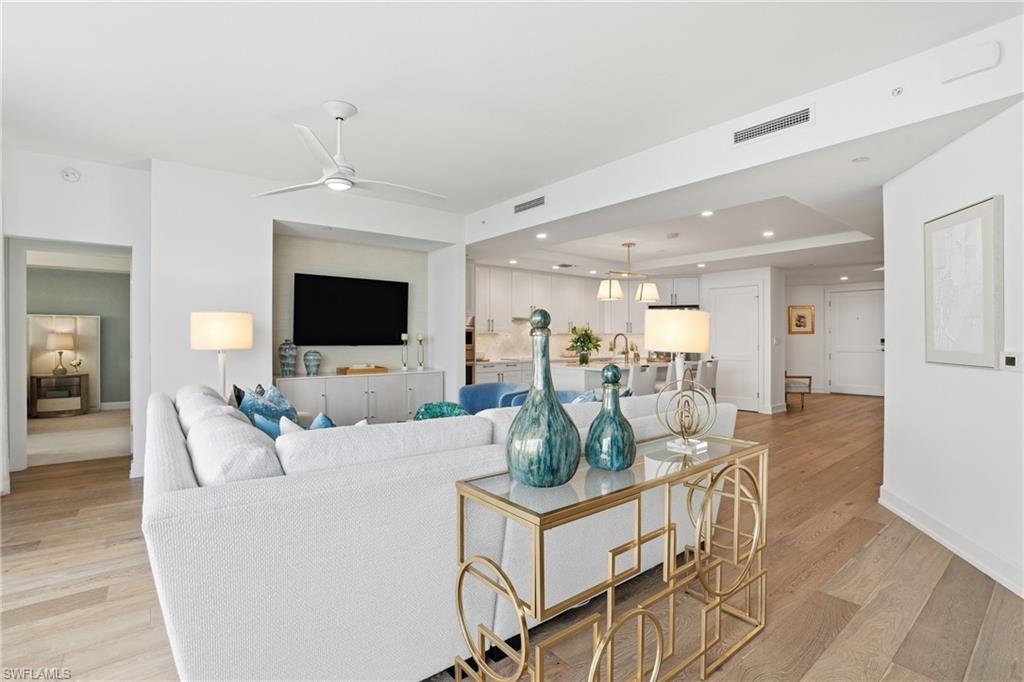 Living area featuring a tray ceiling, light wood-type flooring, recessed lighting, a ceiling fan, and a chandelier - Virtually Edited Image