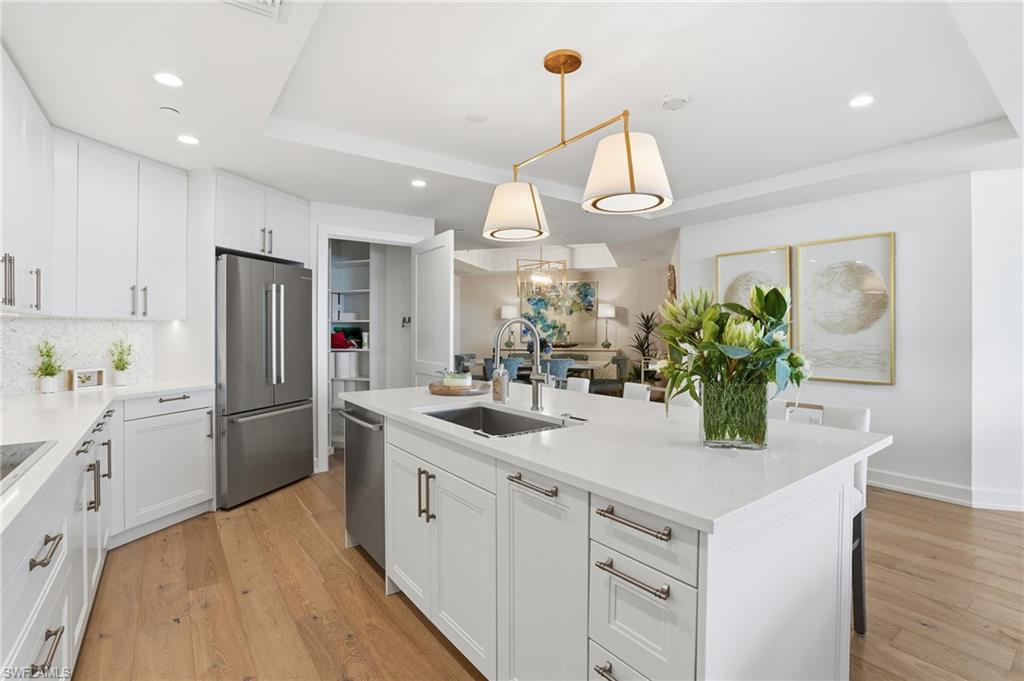 Kitchen with white cabinets, decorative light fixtures, appliances with stainless steel finishes, light wood-type flooring, and a kitchen island with sink - Virtually Edited Image