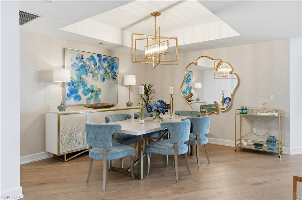 Dining area featuring a raised ceiling, light wood-style flooring, a chandelier, and wallpapered walls - Virtually Edited Image
