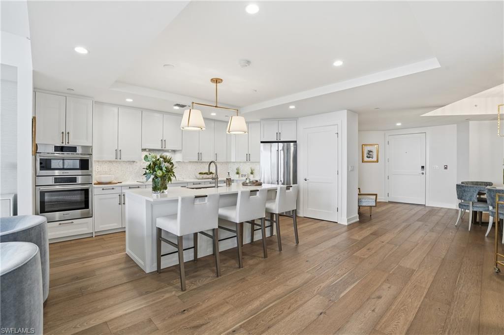 Kitchen with a raised ceiling, a breakfast bar, pendant lighting, a center island with sink, and white cabinetry - Virtually Edited Image