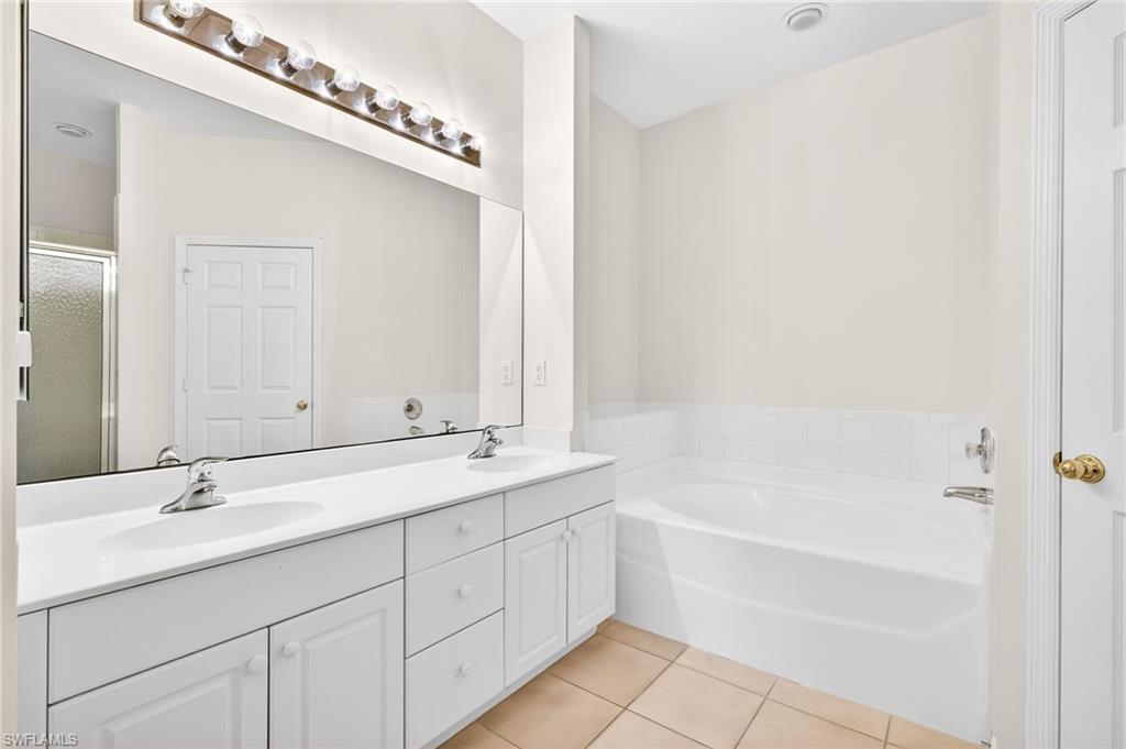 Bathroom featuring double vanity, a shower stall, a garden tub, and light tile patterned flooring