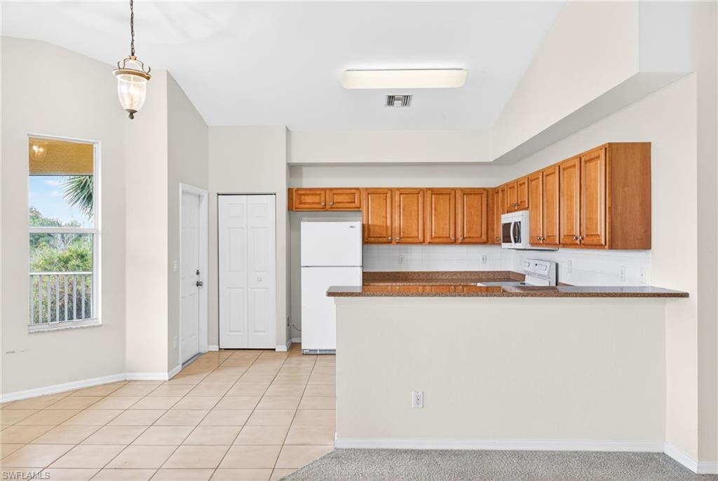 Kitchen featuring brown cabinets, pendant lighting, white appliances, dark stone countertops, and backsplash
