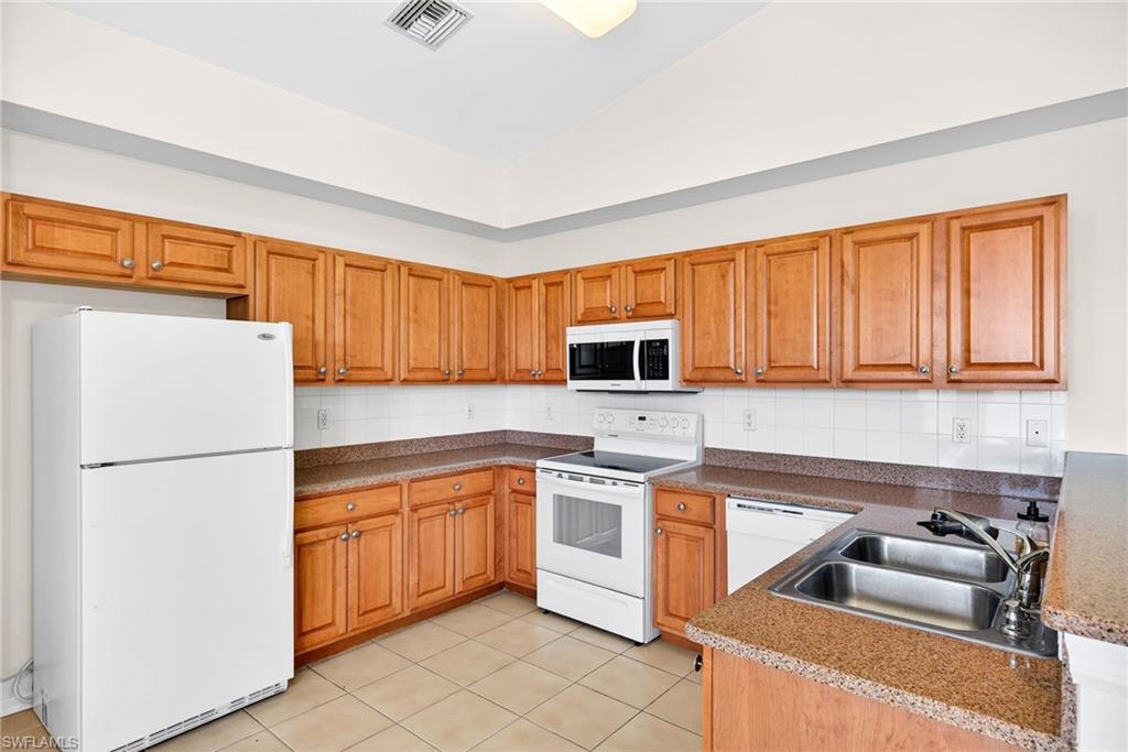 Kitchen with white appliances, lofted ceiling, brown cabinets, backsplash, and light tile patterned floors