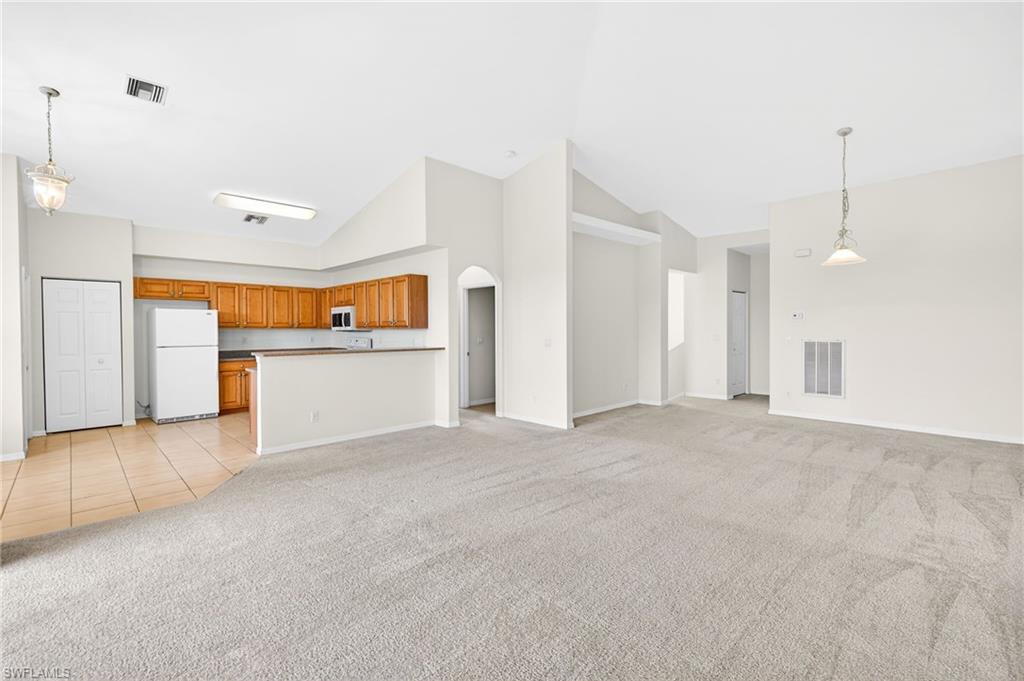 Unfurnished living room with light colored carpet, arched walkways, high vaulted ceiling, and light tile patterned floors