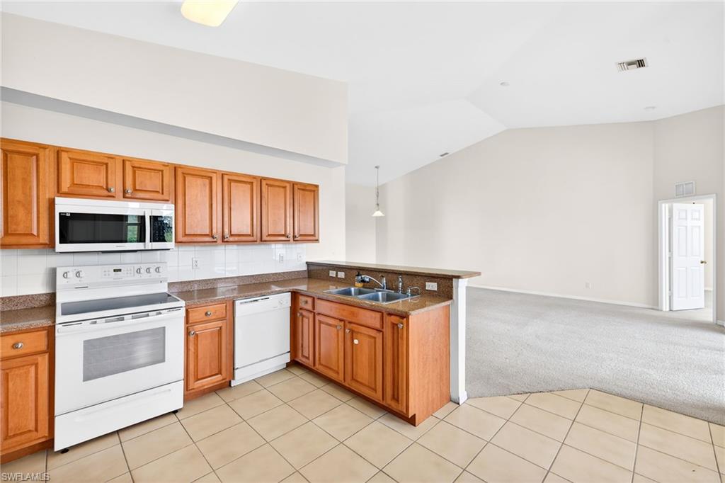 Kitchen featuring light carpet, white appliances, open floor plan, lofted ceiling, and brown cabinets