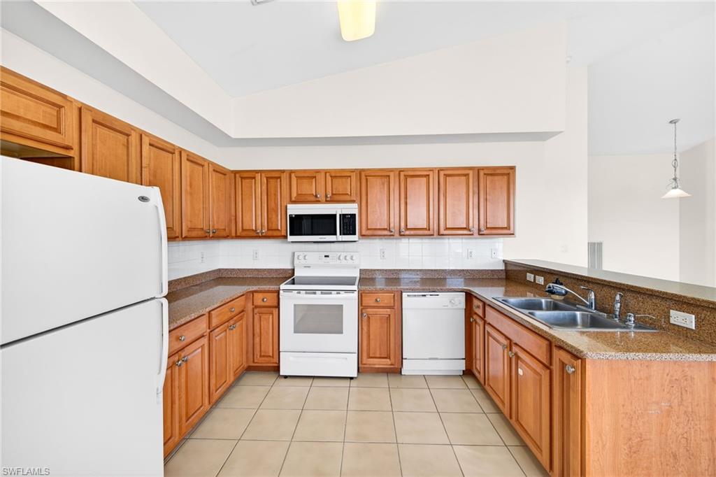 Kitchen featuring white appliances, brown cabinets, a peninsula, hanging light fixtures, and backsplash