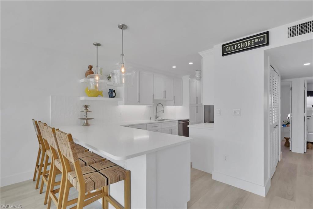Kitchen featuring a breakfast bar area, a peninsula, white cabinets, open shelves, and hanging light fixtures