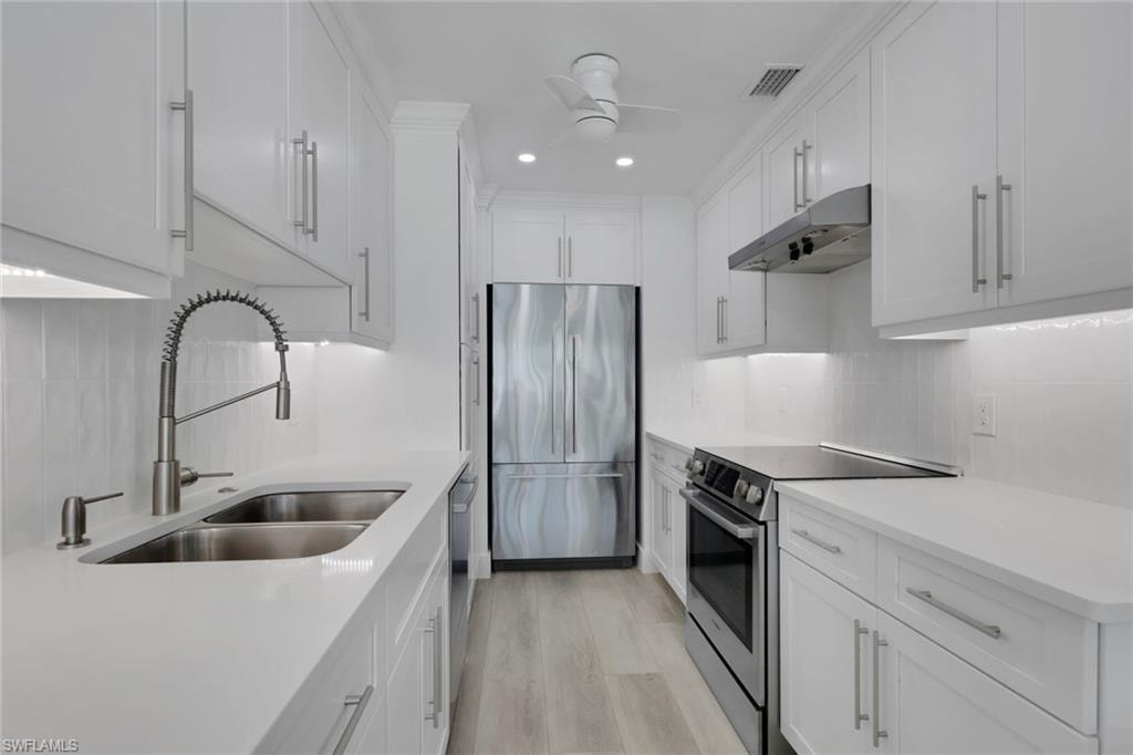 Kitchen with stainless steel appliances, under cabinet range hood, white cabinetry, backsplash, and recessed lighting