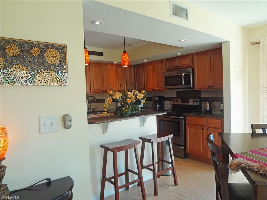 Kitchen featuring a kitchen bar, stainless steel appliances, a peninsula, hanging light fixtures, and brown cabinets