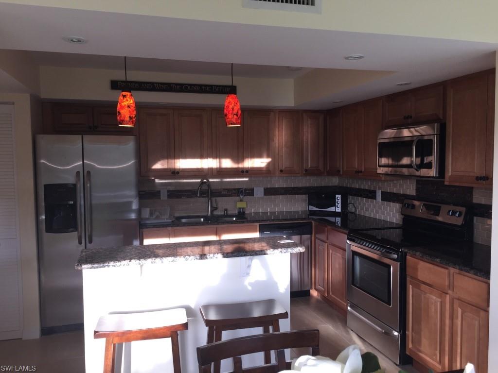 Kitchen featuring appliances with stainless steel finishes, decorative light fixtures, dark stone counters, a breakfast bar area, and tasteful backsplash