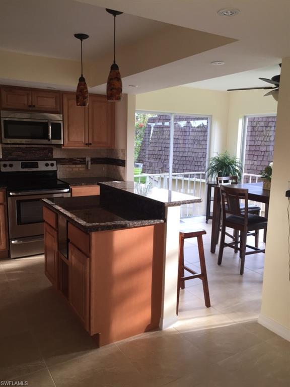 Kitchen featuring stainless steel appliances, decorative backsplash, dark stone countertops, decorative light fixtures, and a breakfast bar area