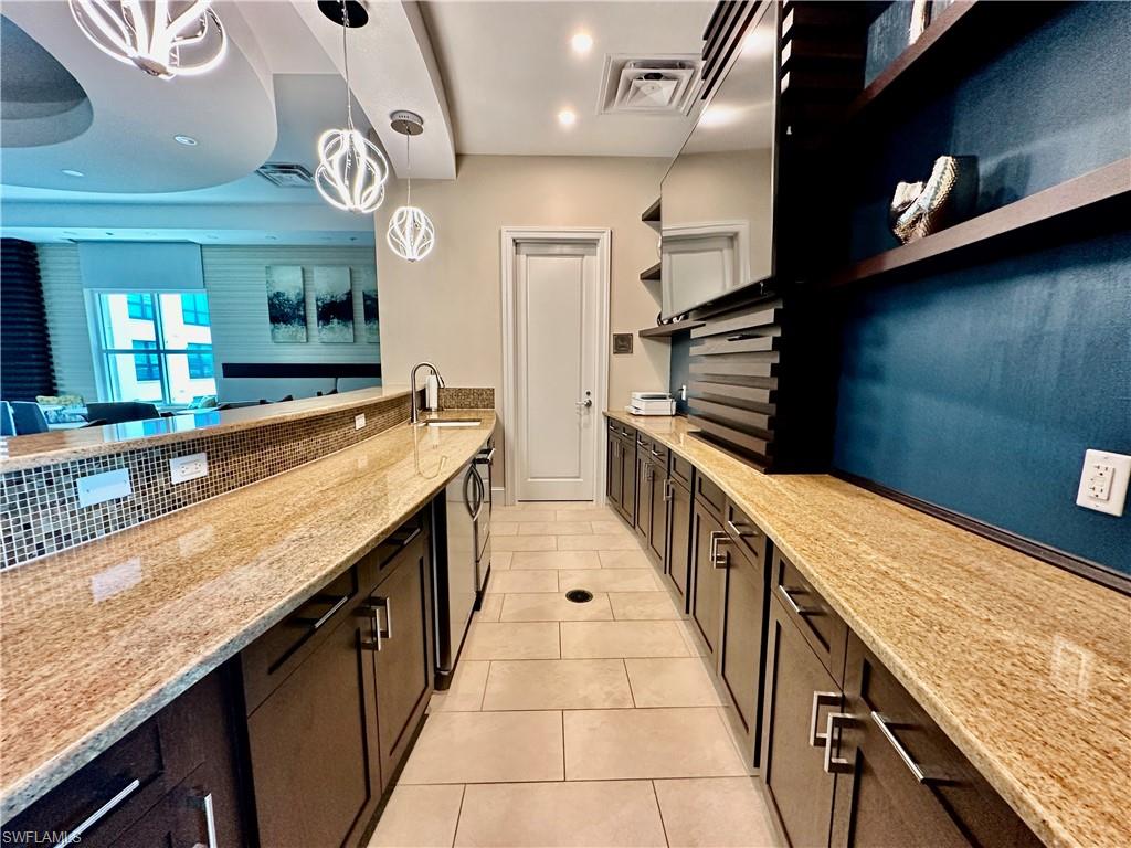 Kitchen with backsplash, decorative light fixtures, light stone counters, sink, and light tile patterned flooring