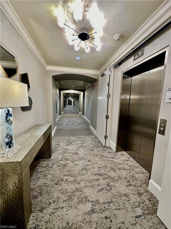 Corridor with crown molding, carpet flooring, an inviting chandelier, and elevator