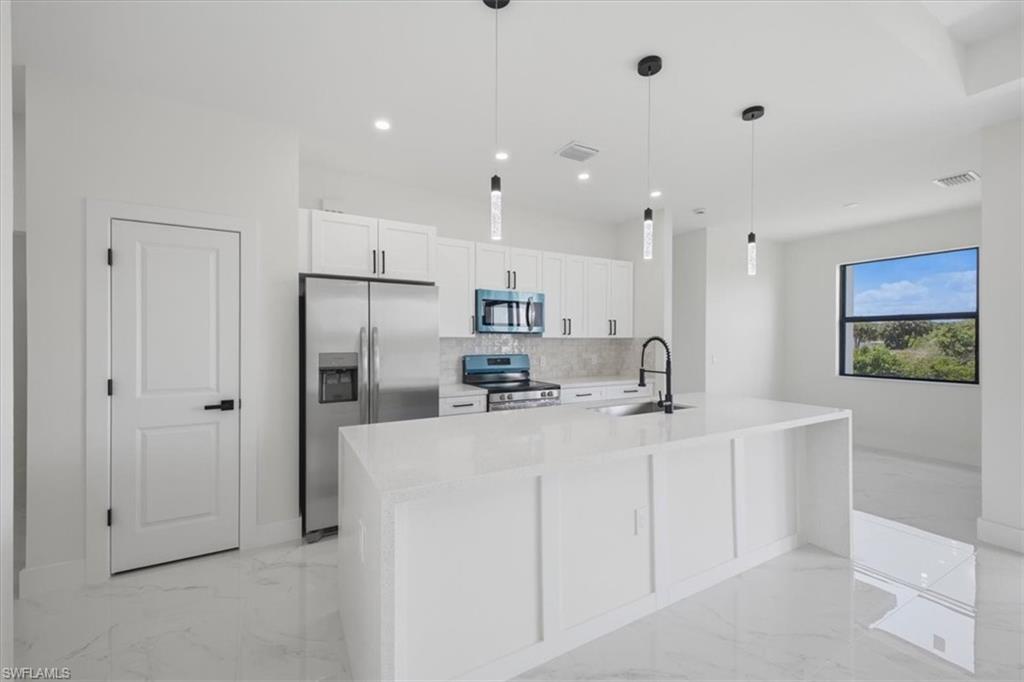 Modern kitchen featuring white cabinetry, stainless steel appliances, a center island with a sink and matte black faucet, pendant lighting, and large format tile flooring