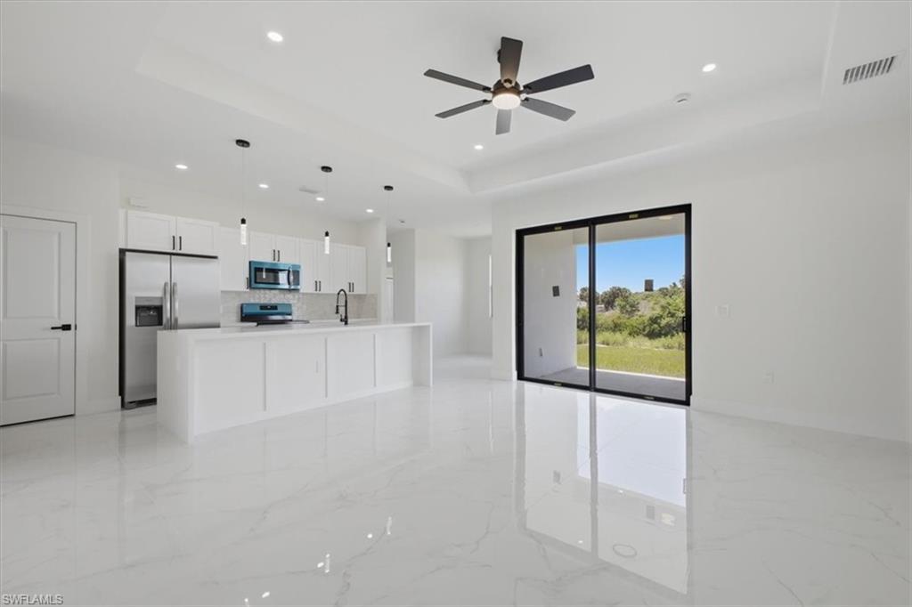 Contemporary kitchen featuring white cabinetry, stainless steel appliances, and a central island with a sink, complemented by polished tile flooring