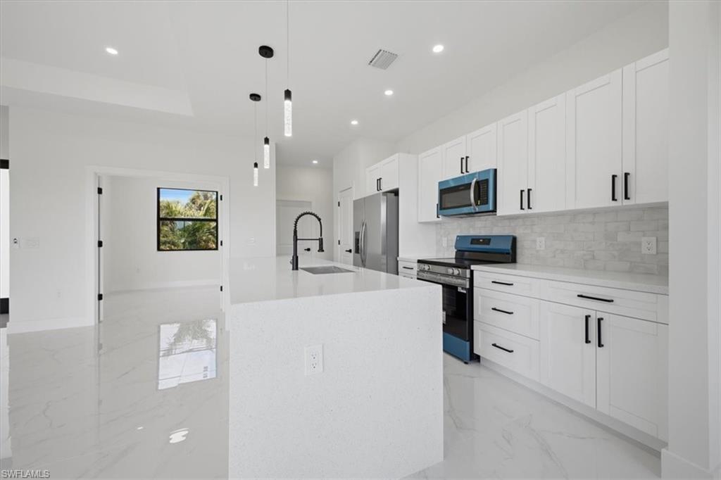 Sleek kitchen featuring white shaker cabinetry with matte black hardware, a light-toned countertop, and a coordinating subway tile backsplash